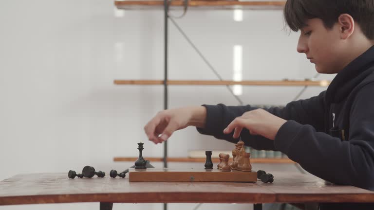 A teenager boy puts chess pieces on the board for the game. Showing interest and intelligence