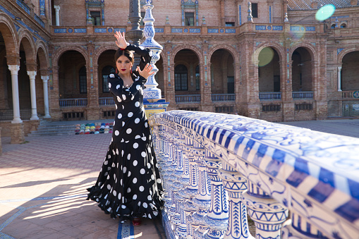 A Hispanic brunette flamenco dancer wearing a white polka dots dress, dancing against an old building in Seville, Spain