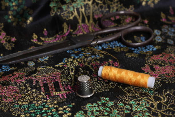 istock Closeup of a thimble with needle and orange thread on vintage Chinese silk. 1467266040