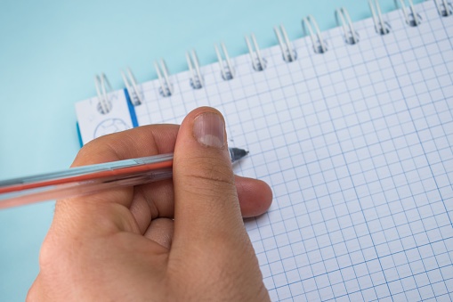 A closeup shot of a person who's about to write on a notebook with a pen