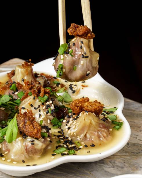 Vertical close-up of chopsticks holding a short rib dumpling with fried pork and sweet ginger sauce