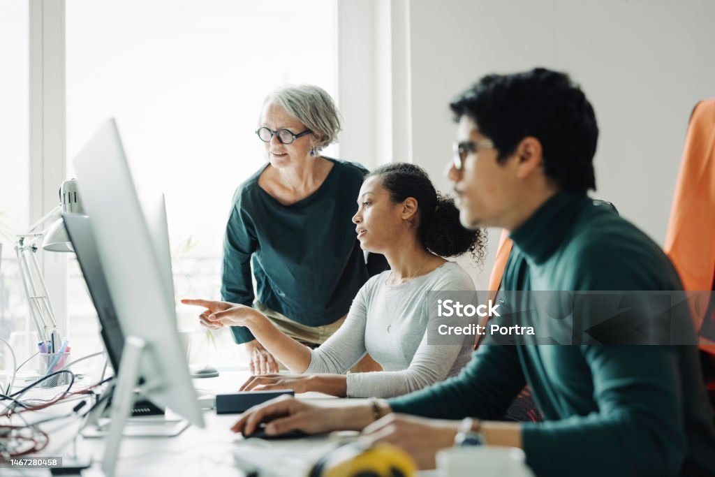 Business people working together in an engineering office Female architects discussing a project looking at computer monitor with a male colleague working in front. Business people working together in an engineering office. Office Stock Photo