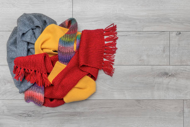 Winter garment accessories, minimal style of white cotton scarf, soft knitted scarf, and casual knitted hat hanging on a coat hook stand against the wall backgrounds.