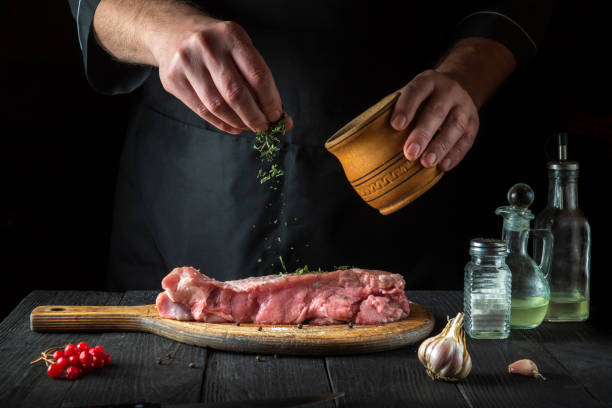 le chef prépare de la viande de veau crue. avant la cuisson, le chef ajoute un assaisonnement sec à base de plantes au bœuf. un plat national est en cours de préparation dans la cuisine du restaurant. - veal calf meat baking photos et images de collection