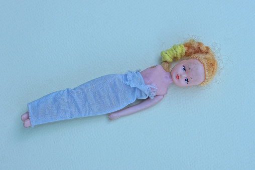 one small plastic old doll without a hand lies on a gray table