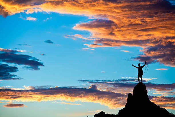 Climber  is silhouetted on the summit of a rock spire in the Sierra Nevada Mountains, California, on a summer day.