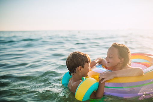 Summer fun at the beach. Four young friends laughing cheerfully while sitting on sea sand at the beach. Group of adorable little kids having a good time together during summer vacation.