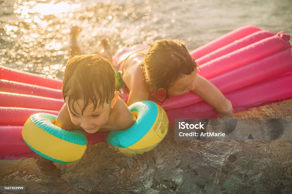Children having fun on summer vacations, swimming, splashing and playing in the sea with inflatable ring Little boy and girl swimming, splashing and playing in the sea with inflatable raft 10-11 Years Stock Photo