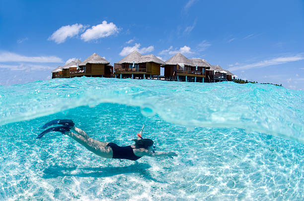 Total tropical II. Split shot of snorkeler swimming in front of water villas in Maldives. diving equipment stock pictures, royalty-free photos & images