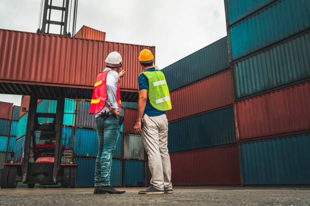 istock Industrial worker works with co-worker at overseas shipping container yard . Logistics supply chain management and international goods export concept . 1467309860