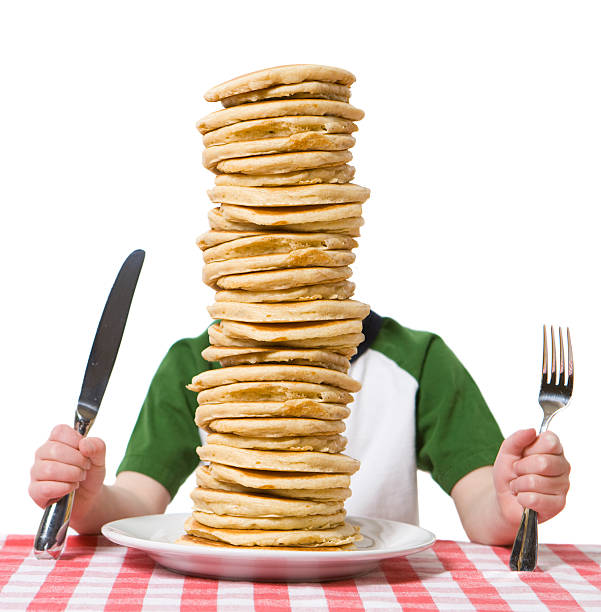 Little boy hidden behind  a giant plate of pancakes, with a knife and fork visible on a table cloth. Please see my other photo with a similar theme, \
