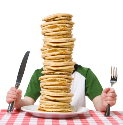 Little boy hidden behind  a giant plate of pancakes, with a knife and fork visible on a table cloth. Please see my other photo with a similar theme, 