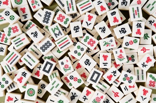 A game of Chinese origin usually played by four persons with tiles resembling dominoes and bearing various designs, which are drawn and discarded until one player wins with a hand of four combinations of three tiles each and a pair of matching tiles.