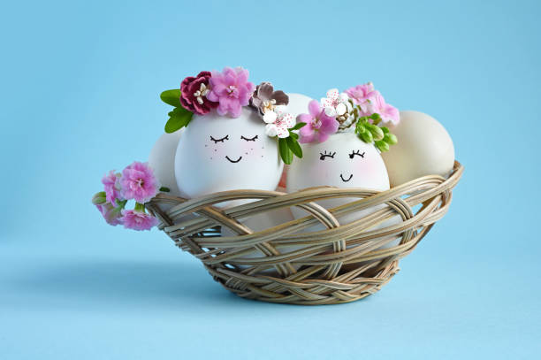istock Natural eggs with drawn smiling face in cute floral crown on blue background. Happy Easter 1467317423