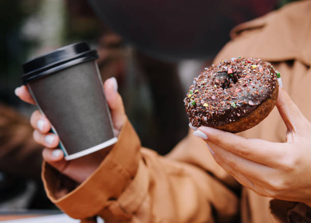 Female hands are holding a donut and a cup of coffee stock photo