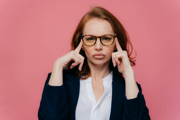 porträt der intensiven schönen dame berührt die schläfen mit beiden händen, versucht, sich an etwas wichtiges zu erinnern, hat einen ernsthaften konzentrierten blick auf die kamera, trägt eine brille und einen eleganten anzug - silence finger on lips businesswoman one person stock-fotos und bilder