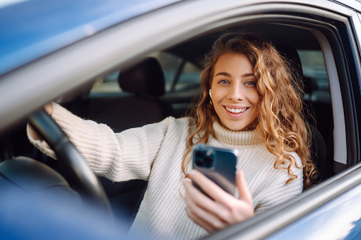 Portrait of a young woman texting on her smartphone while driving a car.