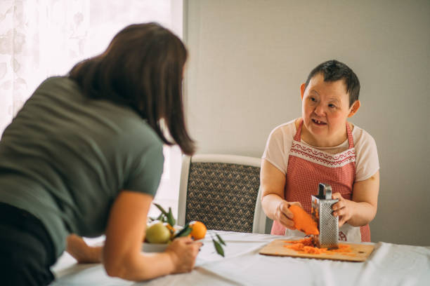 Lifestyle, education. An elderly woman with down syndrome is studying in the kitchen or classroom with a teacher stock photo