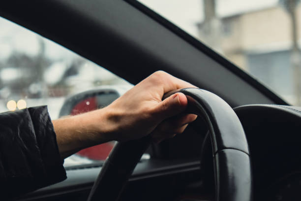 istock Selective focus man's hand on steering wheel, driving car in winter background. Black luxury modern car Interior. Steering wheel, shift lever and dashboard. Black leather Detail Automatic gear stick 1467329608