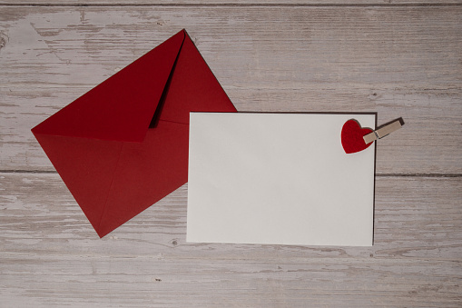 Greeting or invitation card mock up with red envelope on wooden background. Romantic Small hearts Valentine day. Blank paper card copy space for your text. Holiday morning. Top view, flat lay minimalist aesthetic luxury bohemian business branding concept