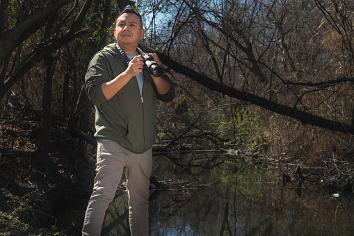 A hispanic man gets ready to take a picture in the woods