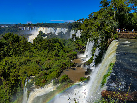 Impressive Iguacu falls, one of the most beautiful waterfalls in the world and one of the seven Wonders of Nature, blurred motion from long exposure at dramatic sunset - Idyllic Devil's Throat - international border of Brazilian Foz do Iguacu city, Parana State, Argentina Puerto Iguazu city, Misiones province and Paraguay - rainforest landscape panorama, South America