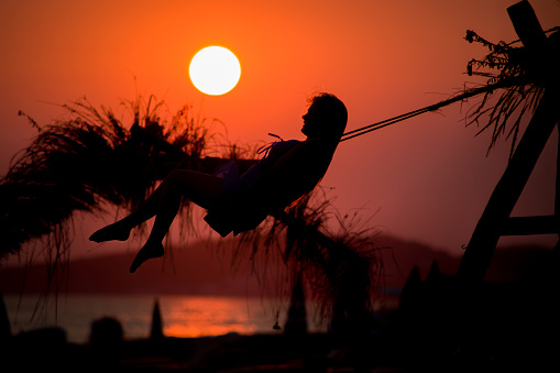 The girl with long hair swinging beside te sea in sunset.