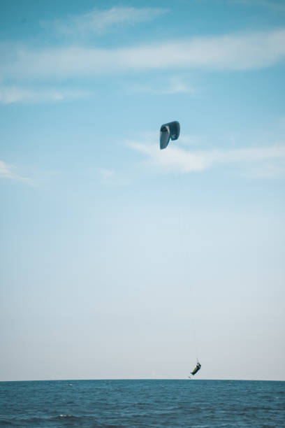 Kite surfer woman holding on to the handle of the kite with one hand and holding on to the surfboard with the other hand while flying in the air against a bright clear sky background
