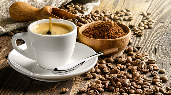 Cup of espresso and coffee beans on old wooden table with coffee powder and wooden scoop. Copy space