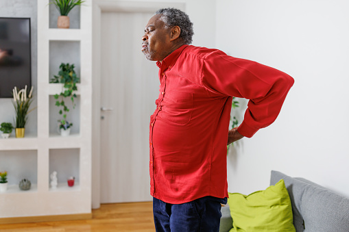 A senior African-American man is standing up and stretching his painful back.