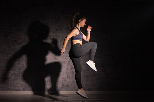Young woman working out with shadow on the wall. Dramatic lighting. Healthy and active lifestyle concept.