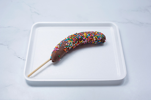 A view of a chocolate covered frozen banana, with rainbow sprinkles.