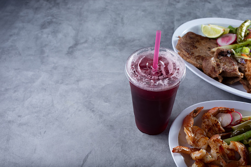 A view of a jamaica agua fresca in a plastic cup, among several Mexican entrees.