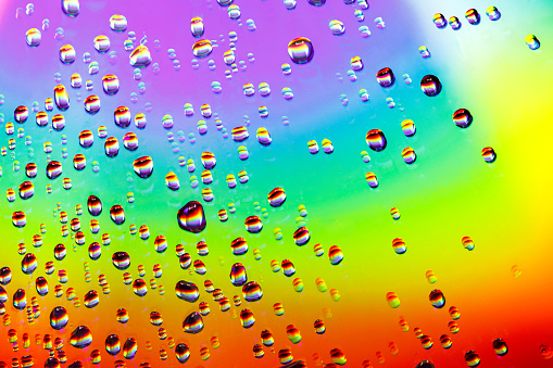 Water drops of different sizes close-up macro on rainbow sparkly mirror polished surface