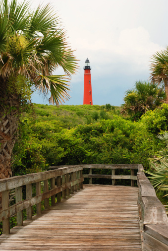 A view of a red lighthouse in the distace from a boardwalk.