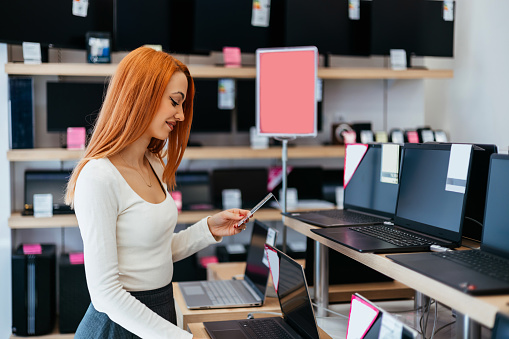 Young dressed woman buying and choosing high quality laptop computer in electronics tech store or shop. Modern people and consumerism concept.