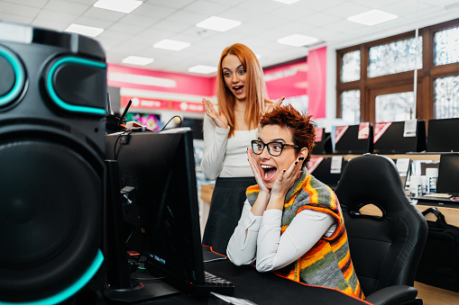Young LGBT lesbian couple buying computer and gaming tech in a modern electronics store. People and consumerism concept.
