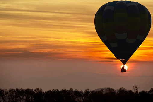 A balloon silhouette is flying over a foggy forest in sunset time
