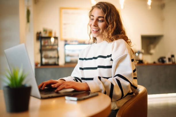 istock Woman sitting in cafe with laptop, typing text message using smart phone while working. 1467364728