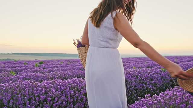 Happy young woman face in lavender field walks spinning smiling in hand straw basket with lavender bouquet in white dress on sunset summer enjoys nature of slow motion. Lifestyle. Travel Relax
