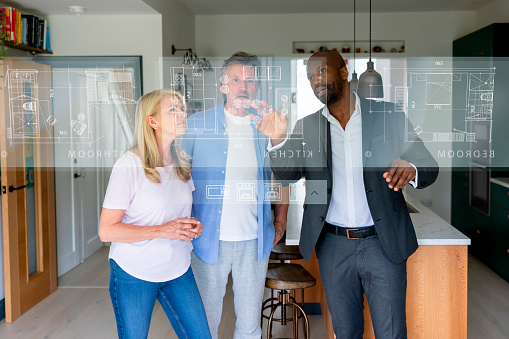 Real estate agent showing a blueprint on a screen to a couple interested in buying a house