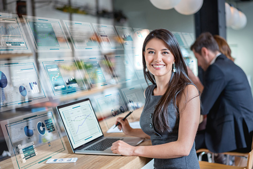 Successful Latin American business woman using technology while working at a cafe and looking at the camera smiling