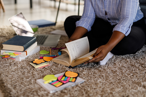 Cut out shot of diligent young woman sitting on the living room floor, flipping pages through the book while studying.