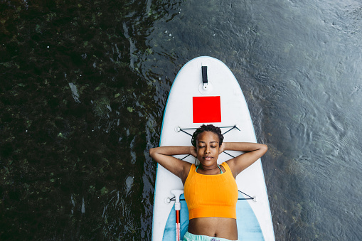 Photo of a young African-American daydreaming while riding standup paddle board on the river