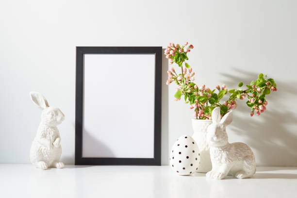 Mockup with a black frame and spring flowers in a vase, easter eggs on a light background. Empty poster frame mockup for presentation design, text, lettering