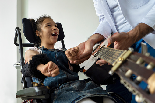 Disabled girl in wheelchair performing music therapy treatment with the help of a music therapist at the comprehensive rehabilitation center for people with disabilities.