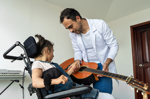 Disabled girl in wheelchair performing music therapy treatment with the help of a music therapist at the comprehensive rehabilitation center for people with disabilities.