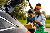 istock Young woman opening car trunk to load groceries with a help of her friend 1467380986