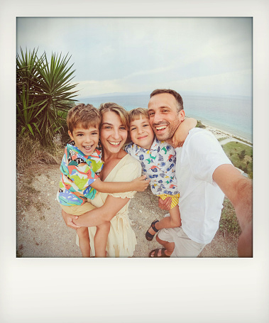 Photo of a smiling family taking a selfie from the hill over the beach during their summer vacation