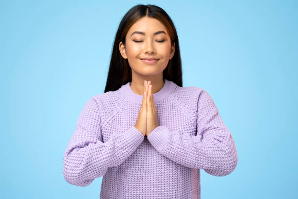 Gorgeous woman keeps hands in yoga gesture, has calm facial expression